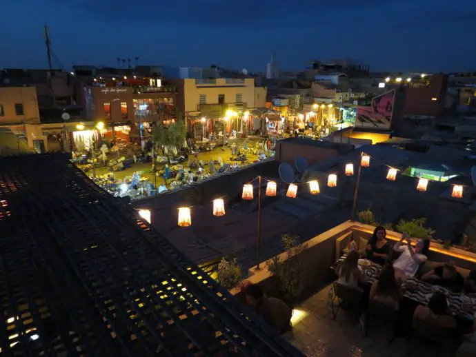 Roof terrace restaurant in Marrakech with string of lanterns overlooking a small square with market stalls
