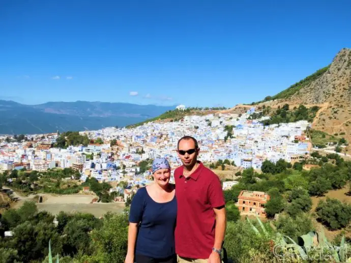 Two people posing for a photograph against a backdrop of a hillside city