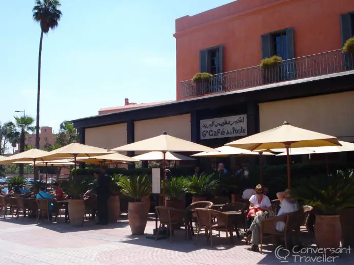 Diners eating at tables beneath parasols on the street outside a large red building