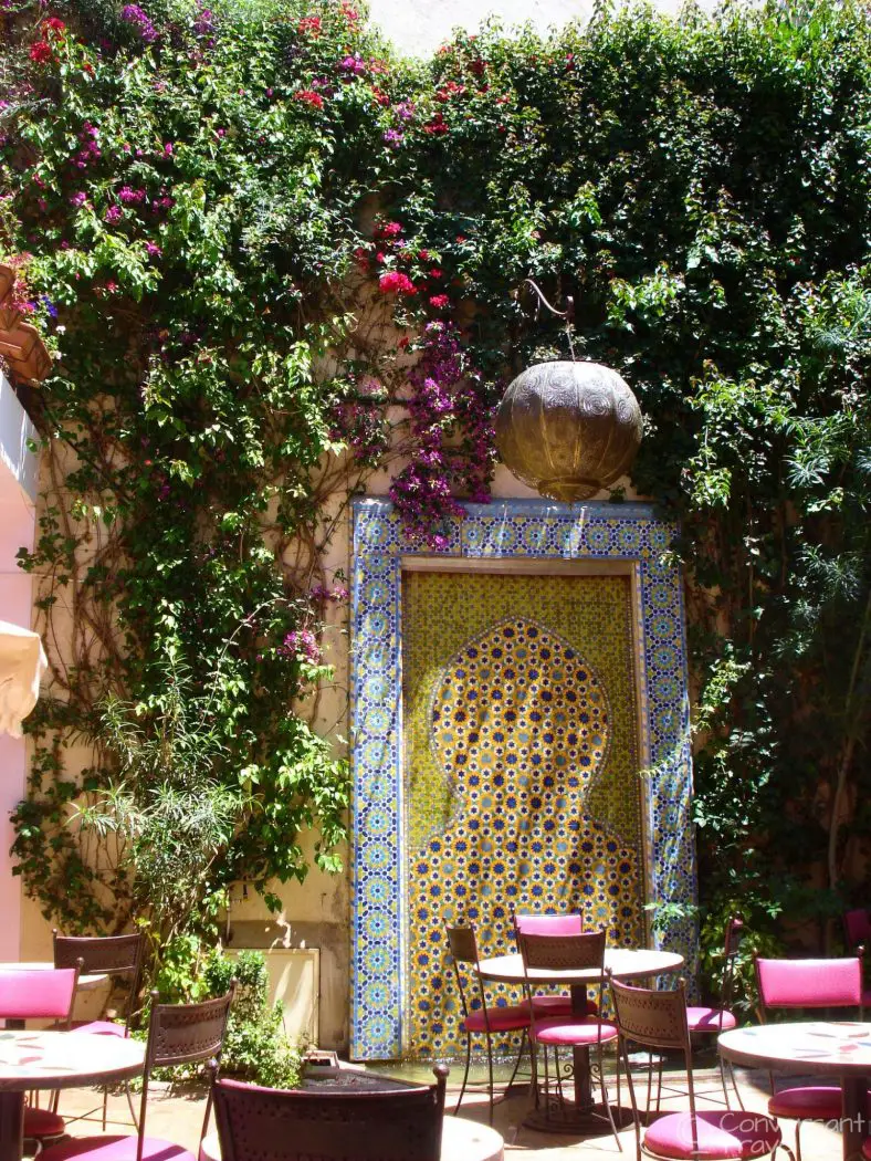 Small cafe seating area with red chairs, a mosaic fountain and lots of foliage