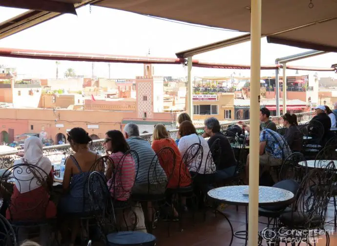 People sitting at tables on a cafe balcony overlooking a city square