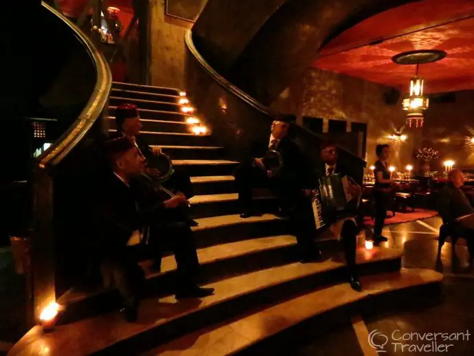 Four musicians sitting on a staircase inside a dimly lit dining rooms with red lighting