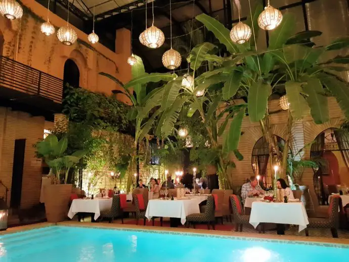 Restaurant tables beside a pool with Moroccan lanterns hanging from the roof