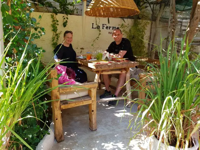 Wooden table and chairs in leafy garden with two people sitting smiling