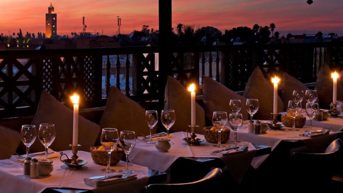 Fine dining at tables with candles on a balcony overlooking a city skyline
