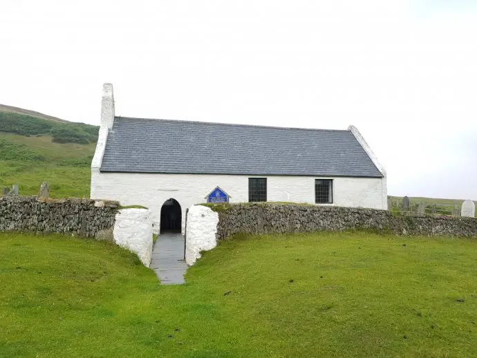 White stone chapel surrounded by a low stone wall in a field of grass