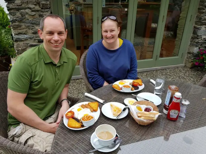 Two people sitting at a table posing beside cooked breakfasts - Glamping in Wales