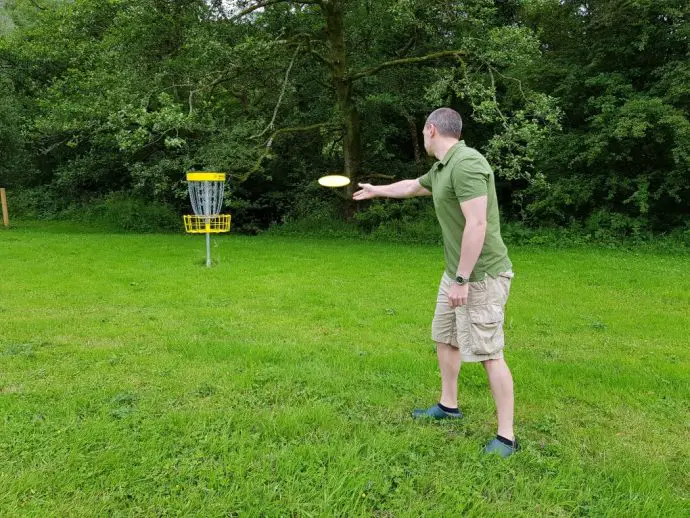 Man in green top throwing yellow frisbee towards a yellow marker post in a field