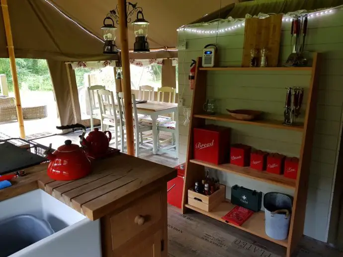 Kitchen area inside a glamping safari tent, with red kettle and red food bins on shelves - Glamping in Wales