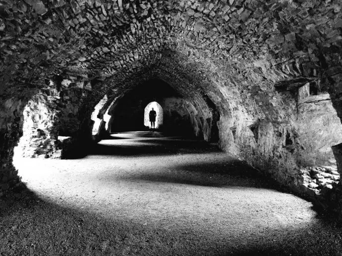 Dark vaulted ceiling hall ruin made of stone with light cascading through the window holes - glamping in Wales