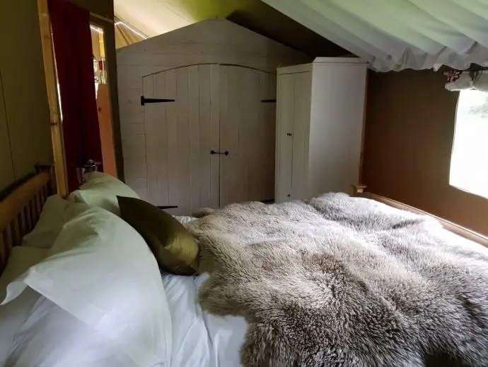 double bed with white sheets and a sheepskin thrown over the top - glamping in Wales