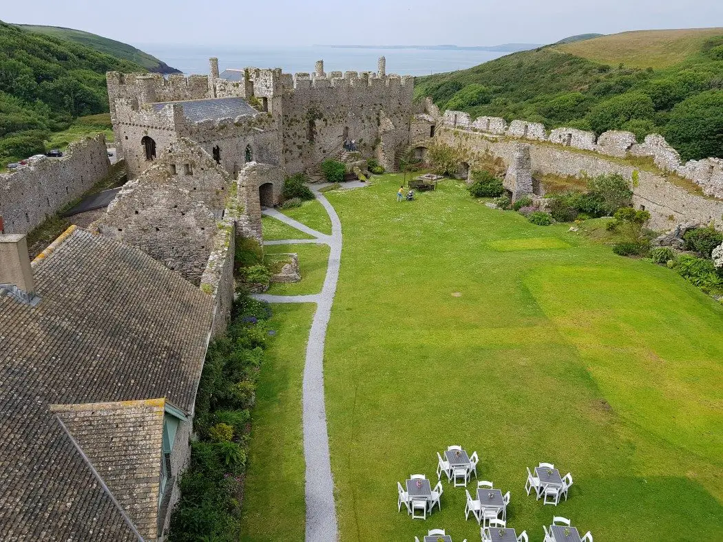 Ruined castle walls surrounding a green lawn area and the sea in the distance