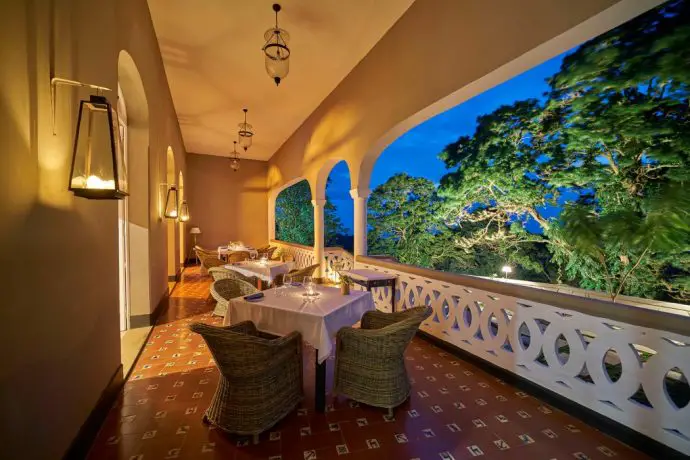 Balcony of a plantation house hotel with chairs and tables set up for dinner, and a view out over tropical forest