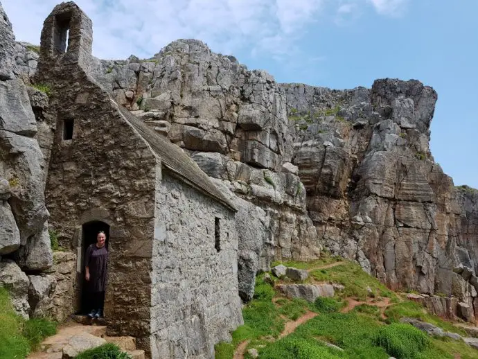 Close up shot of stone chapel built into the side of a cliff with a path running alongside to the right