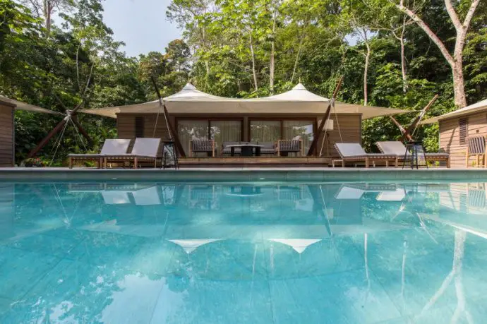 Luxury tented room with pool in foreground, surrounded by white sunloungers