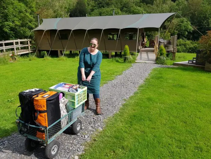 Woman pulling a small cart full of luggage down a path towards a glamping safari tent