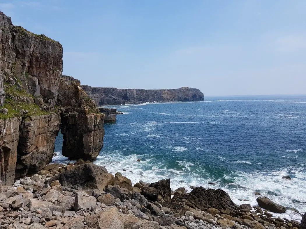 High cliffs and a tall sea arch on the left, with sea to the right, and a rocky foreground