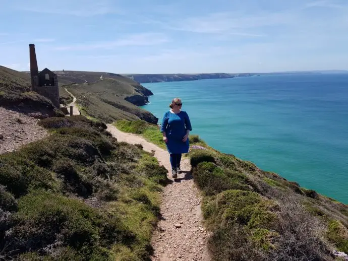 woman walking along a coastal path with a tin mine in the background