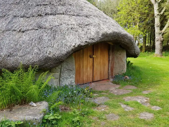 Close up of wooden front door of an Iron Age roundhouse with a thatched roof - romantic places to stay in Cornwall