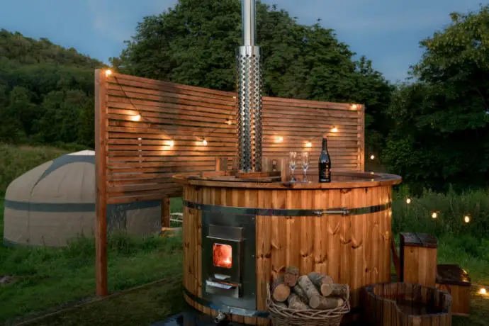 Round wooden hot tub with yurt in the distance - Lake District Glamping site