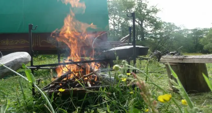 Outdoor log fire in front of a bow top caravan