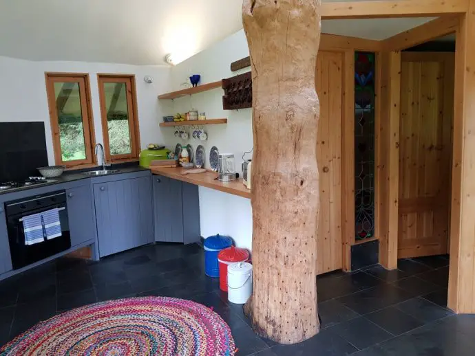 Kitchen and bathroom area inside a cabin with a tree trunk growing through the middle