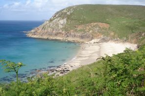 Moon shaped beach with rocky headland in the background, grass in the foreground and sea to the left - Portheras Cove in Cornwall