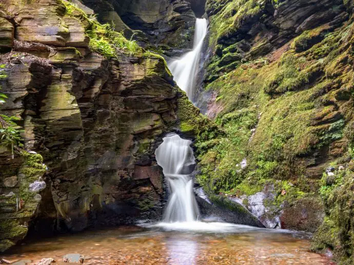 waterfall surrounded by steep rock cliffs covered in green moss - unusual things to do in Cornwall