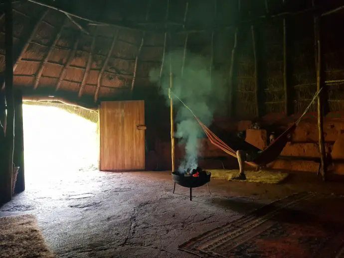 Dark interior of a roundhouse, with man in a hammock and a fire pit - romantic places to stay in Cornwall