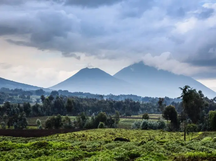 Distant misty volcanoes with green forests and fields in the foreground