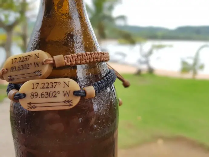 two bracelets hanging around the neck of a beer bottle on a beach