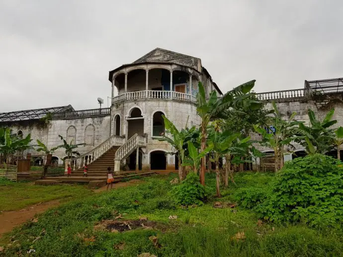 Old ruined white colonial building surrounded by lush foliage