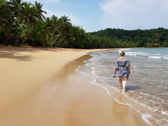 Woman walking along beach with sea to the right and palm trees to the left