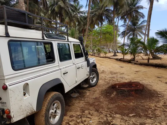 White landrover parked on a beach surrounded by palm trees
