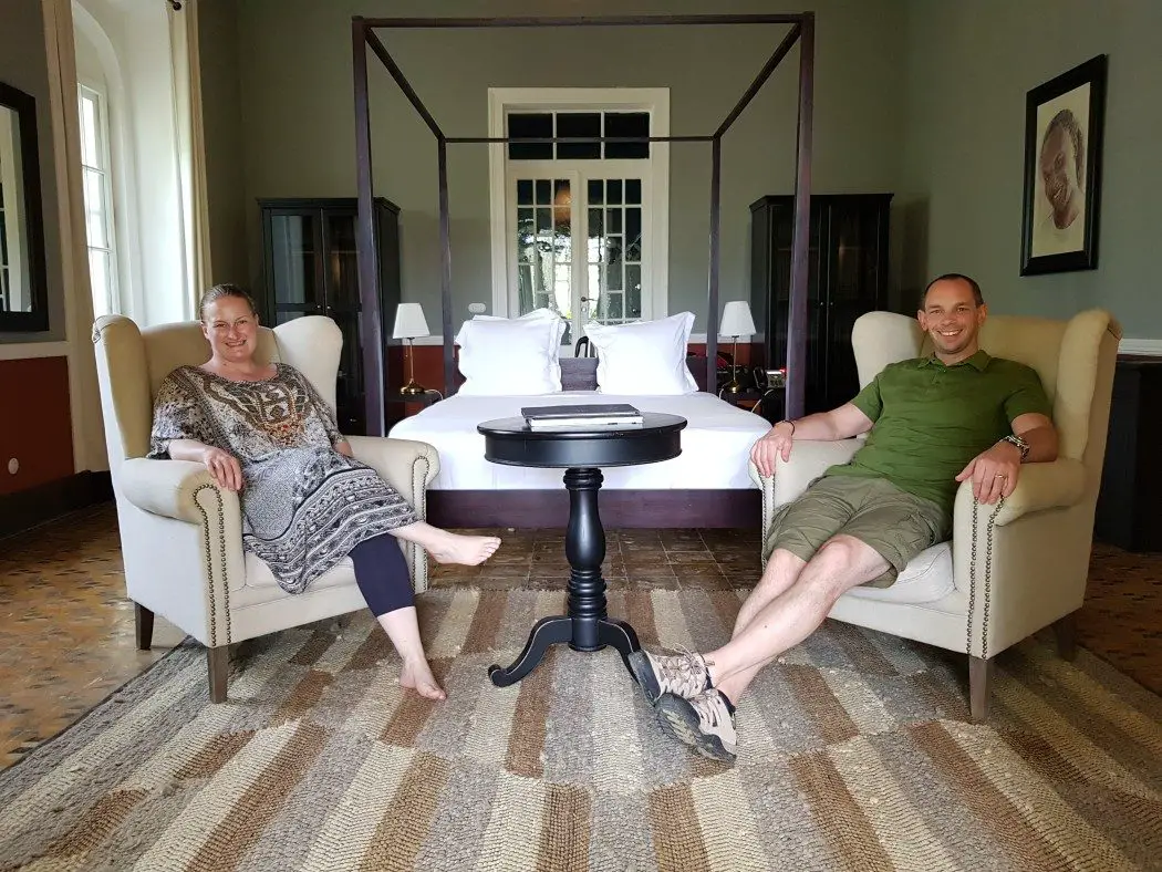 Bedroom with 4 poster bed, and 2 people sitting in armchairs in front of it