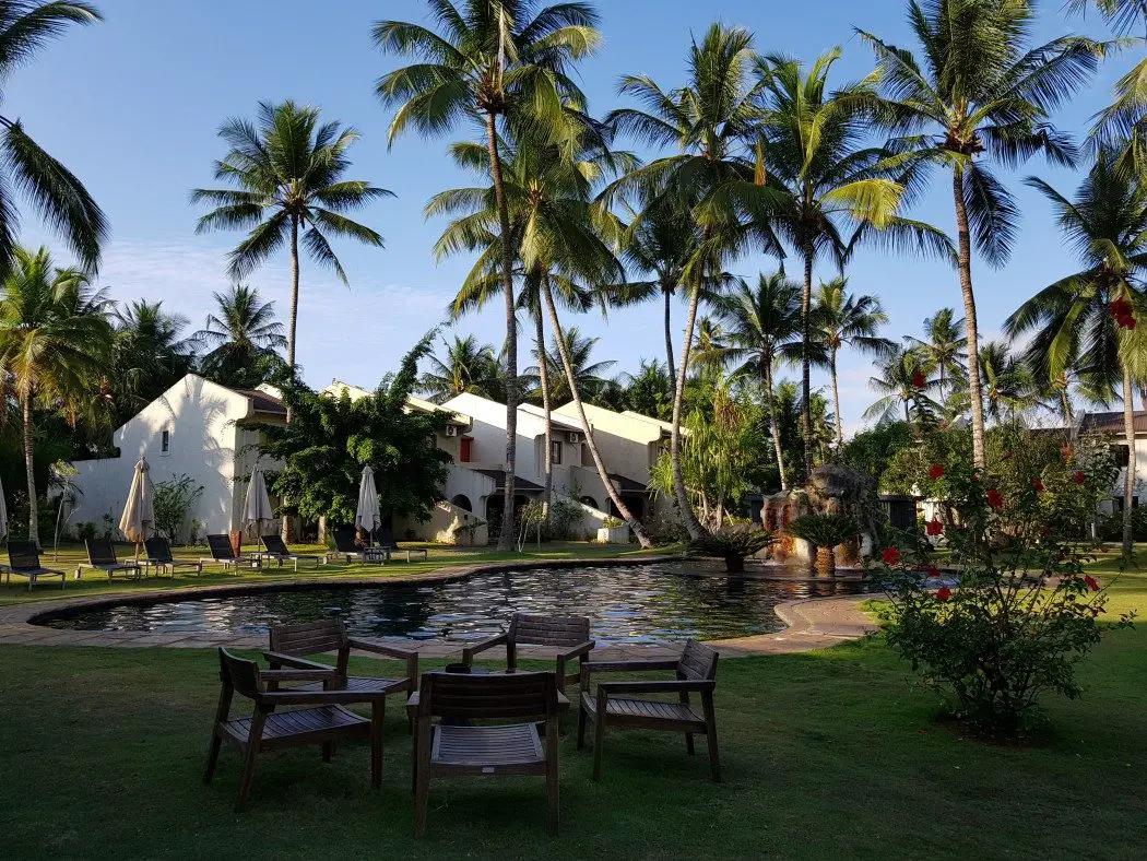 White hotel buildings beside a pool surrounded by palm trees