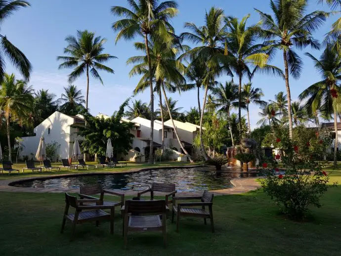 White hotel buildings beside a pool surrounded by palm trees