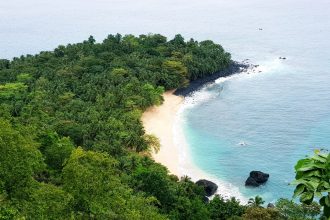 Aerial view of banana shaped beach with rainforest to the left and ocean to the right