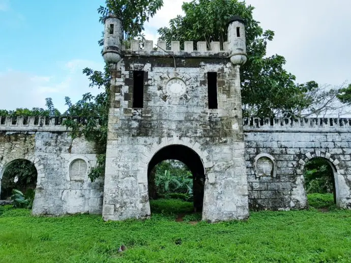 ruined building with archway and castellated tower top surrounded by forest