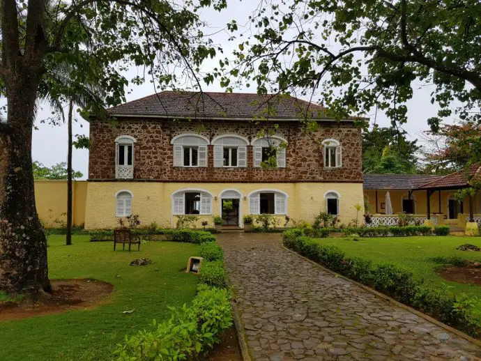 An old colonial house with yellow and brick facade in tropical gardens