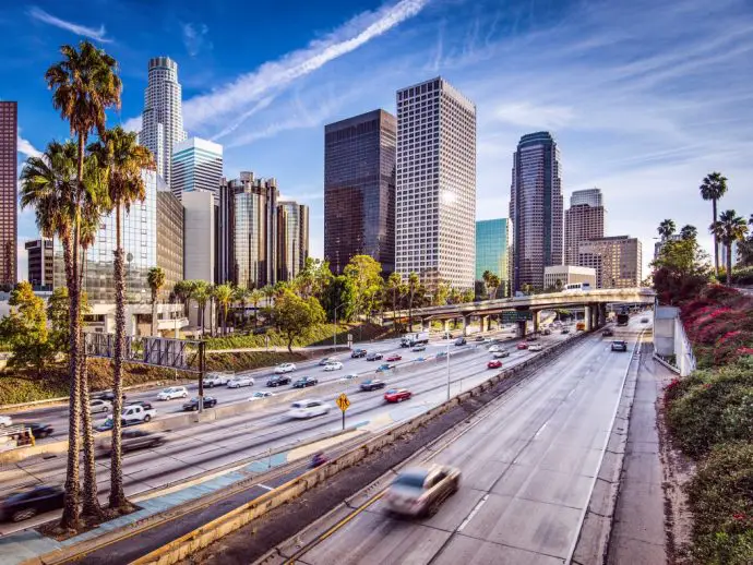 Tall high rise buildings with large multi-carriageway road leading up to them, with palm trees on the left