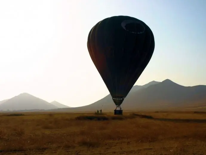 Hot air balloon inflated but on the ground in front of some distant mountains