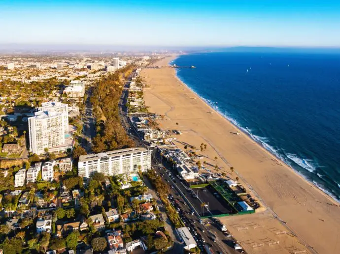 Aerial view of long stretch of beach with buildings to the left and blue ocean to the right