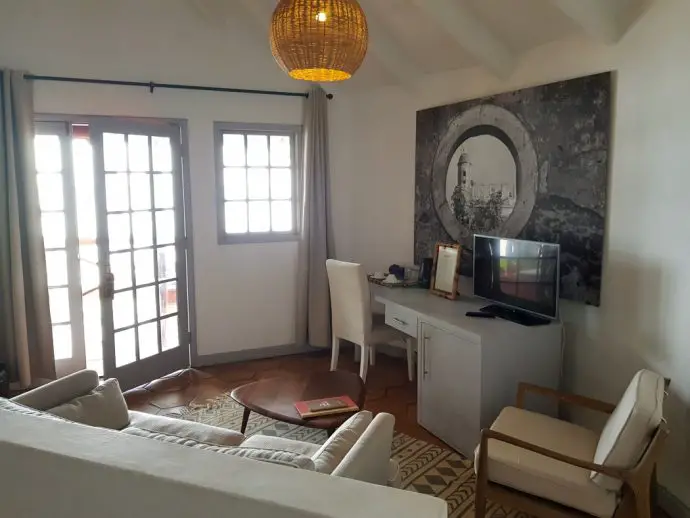 Lounge area in a bedroom with white chairs, white desk, tv and a black and white picture on the wall