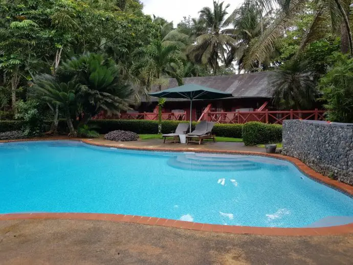 Swimming pool with deck chairs and a wooden bungalow behind