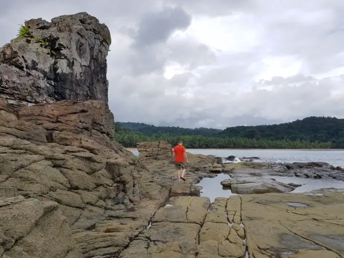 Man in orange shirt scrambling on rocks looking out to sea