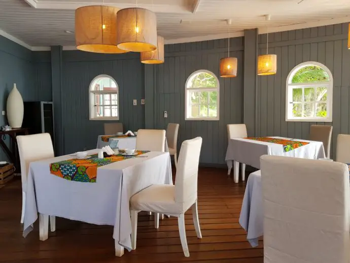 Restaurant dining room with tables and chairs with white table clothes and rattan ceiling lamps