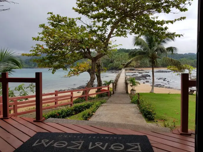 Wooden walkway over the sea with beach in distance and trees in foreground