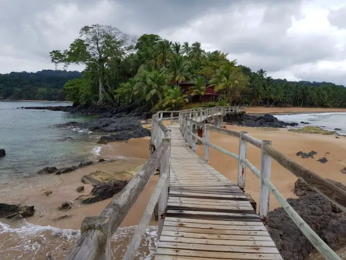 Wooden walkway over sea and sand leading to a small forested island