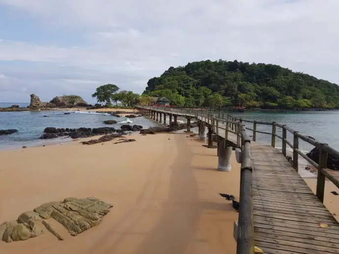 Wooden walkway over the sea towards a small island covered in tropical forest